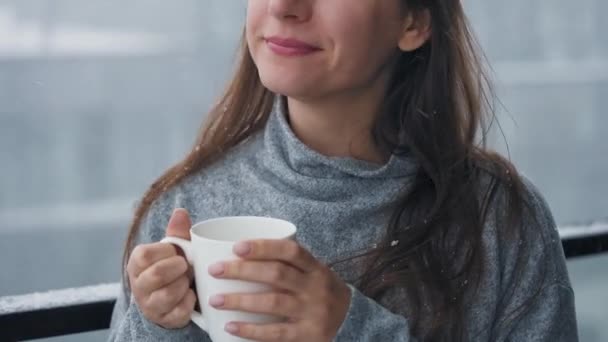 Frau bleibt bei Schneefall mit heißem Kaffee oder Tee auf Balkon Sie blickt auf die Schneeflocken und atmet die frostige frische Luft ein. — Stockvideo