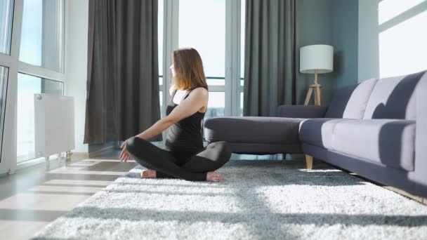 Ung kaukasisk kvinna i svart overall gör yoga hemma för att utveckla flexibilitet och balans. — Stockvideo