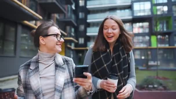 Δύο ευτυχισμένες γυναίκες περπατούν με καφέ και μιλάνε με ενδιαφέρον μεταξύ τους στην επιχειρηματική περιοχή. Αργή κίνηση — Αρχείο Βίντεο
