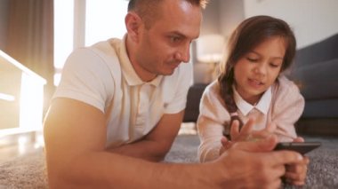 Baba ve kızı birlikte vakit geçiriyorlar ve evde oturma odasında yerde yatarken aile eğlencesi için tablet kullanıyorlar..
