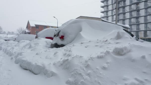 雪の吹雪の後に雪に覆われた車。バックグラウンドでの住宅建築. — ストック動画