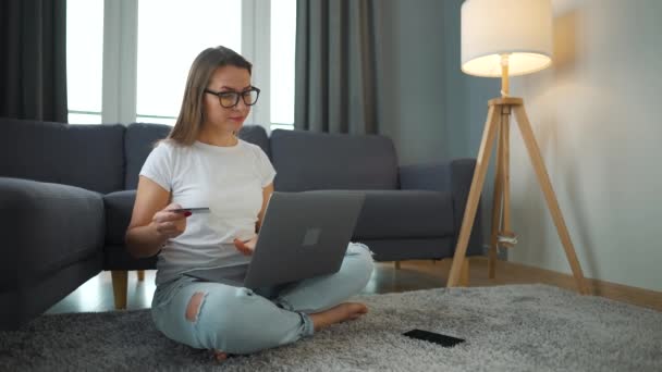 Donna con gli occhiali è seduto sul pavimento e fa un acquisto online con carta di credito e smartphone. Shopping online, tecnologia lifestyle — Video Stock