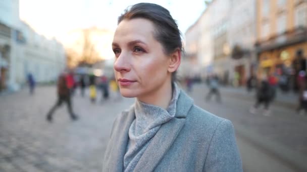 Portret van een blanke vrouw in een jas midden op het oude stadsplein. Ze kijkt naar de camera en zet een bril op.. — Stockvideo