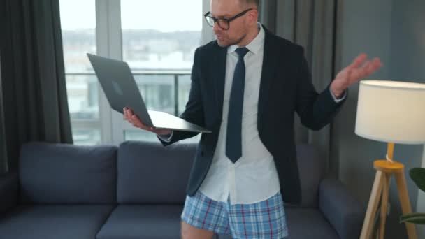 Caucasian man dressed in a jacket and underwear using laptop to make a video call from home in a modern apartment. Remote work during a pandemic — Stock Video