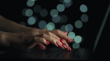 Kadın eller geceleri dizüstü bilgisayarda yazıyorlar. Arkaplanda bulanık ışıklar