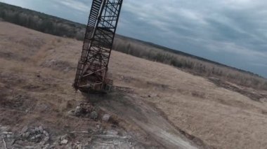 FPV insansız hava aracı, terk edilmiş sanayi binaları ve bir kazıcının etrafında hızla ve manevra kabiliyetiyle uçar..