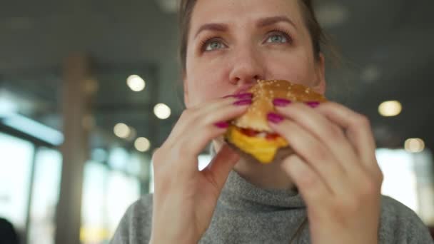 O femeie care mănâncă hamburger şi cartofi prăjiţi într-o cafenea. Burger în mâini de femeie . — Videoclip de stoc
