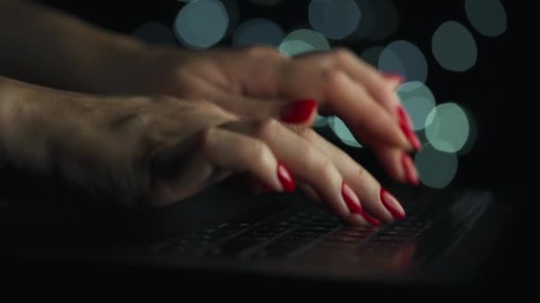 Kadın eller geceleri dizüstü bilgisayarda yazıyorlar. Arkaplanda bulanık ışıklar — Stok video