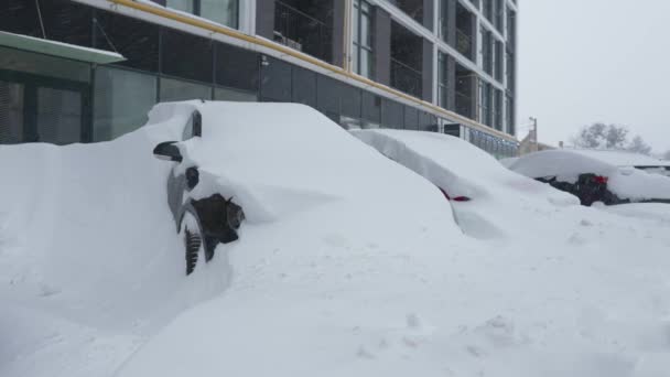 Coches cubiertos de nieve después de una ventisca de nieve. Edificio residencial en el fondo. — Vídeos de Stock