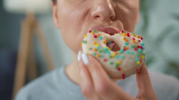 Mujer comiendo una rosquilla dulce en esmalte blanco con aspersiones multicolores. Primer plano — Vídeos de Stock