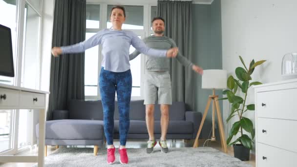 Caucásico pareja está haciendo saltos gatos ejercicio en casa en acogedora habitación luminosa, cámara lenta. — Vídeos de Stock