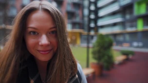 Retrato de una hermosa mujer morena sonriendo encantadoramente mientras estaba de pie sobre el fondo de los edificios modernos. La joven feliz disfruta de la vida. Movimiento lento — Vídeos de Stock