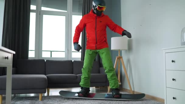 Vtipné video. Muž oblečený jako snowboardista zobrazuje snowboarding na koberci v útulné místnosti. Čekám na zasněženou zimu. Zpomalený pohyb — Stock video