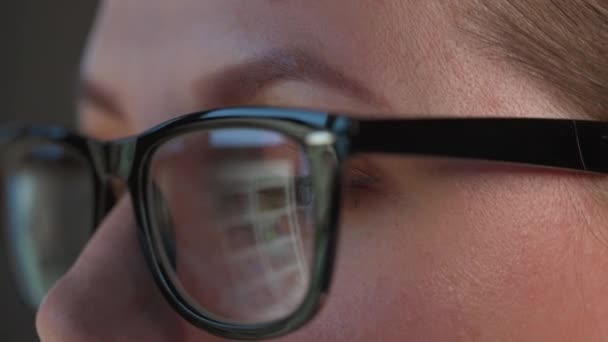 Frau mit Brille blickt auf den Monitor und surft im Internet. Der Monitor-Bildschirm spiegelt sich in der Brille wider. Arbeiten in der Nacht. Innenministerium. Fernbedienung — Stockvideo