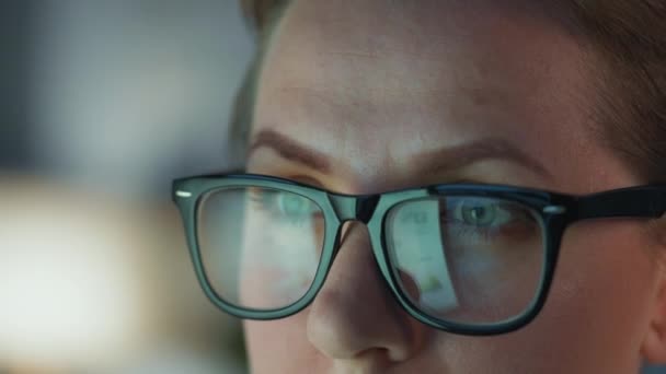 Mujer con gafas mirando en el monitor y trabajando con gráficos y análisis. La pantalla del monitor se refleja en las gafas. Trabaja de noche. Primer plano extremo — Vídeo de stock