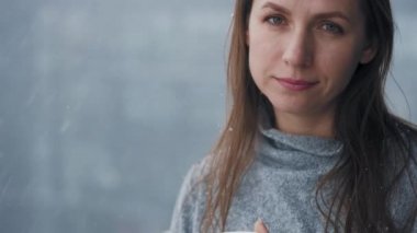 Beyaz kadın kar yağışı sırasında sıcak kahve ya da çayla balkonda kalır. Kar tanelerine bakıyor ve soğuk temiz havayı soluyor.