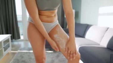 Kadın bacağına anti-selülit kremi sürüyor ve kendine masaj yapıyor.