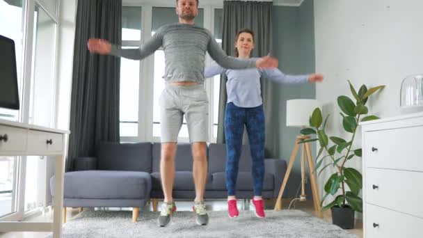 Caucasian couple is doing jumping jacks exercise at home in cozy bright room, slow motion. — Stock Video