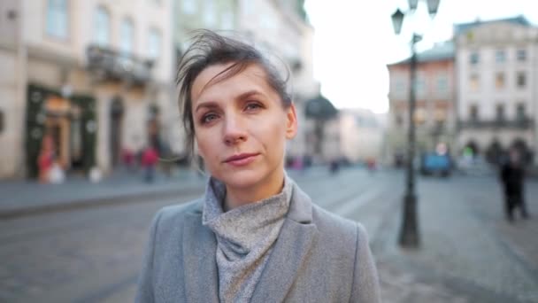 Portrait d'une femme caucasienne vêtue d'un manteau au milieu de la place de la vieille ville. Elle regarde sérieusement la caméra.. — Video