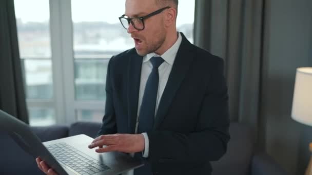 Biały mężczyzna ubrany w kurtkę i bieliznę, korzystający z laptopa, by wykonać wideo rozmowę z domu w nowoczesnym mieszkaniu. Praca zdalna podczas pandemii — Wideo stockowe