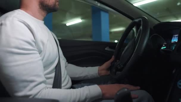 Hombre conduciendo coche a través de un estacionamiento subterráneo y está buscando un lugar para aparcar o se aleja. Vista lateral — Vídeo de stock