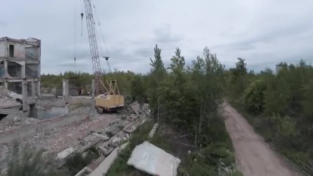 El dron FPV vuela rápido y maniobrable entre edificios industriales abandonados y alrededor de una excavadora. — Vídeo de stock