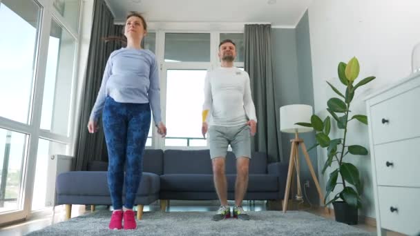 Couple caucasien fait des sauts jacks exercice à la maison dans une salle lumineuse confortable, au ralenti. — Video