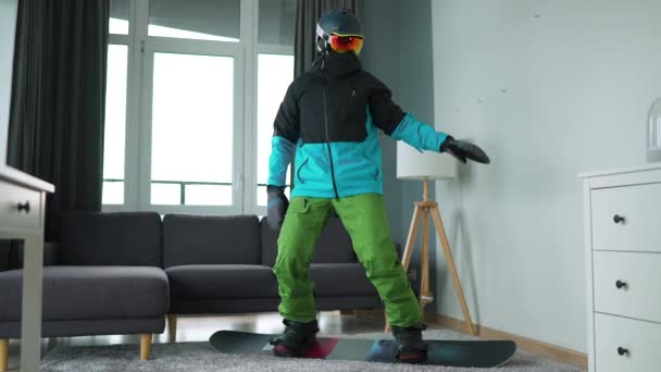 有趣的视频。打扮成滑雪者的人在舒适的房间里把滑雪板放在地毯上。等待着一个多雪的冬天。慢动作 — 图库视频影像