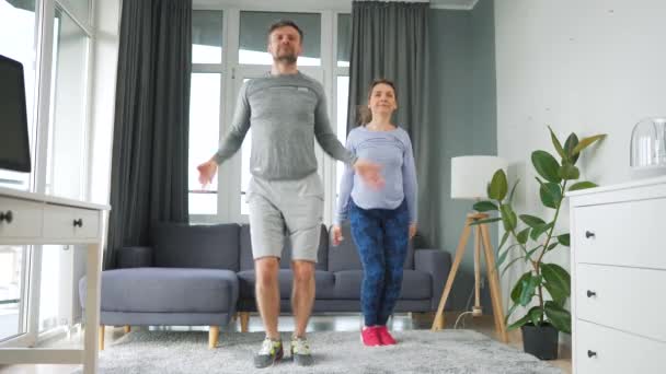 Caucásico pareja está haciendo saltos gatos ejercicio en casa en acogedora habitación luminosa, cámara lenta. — Vídeos de Stock