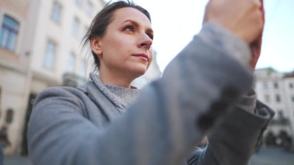 Жінка в пальто, що стоїть посеред старої площі, використовує смартфон і фотографує. Повільний рух — стокове відео