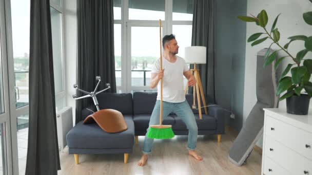 Homem limpando a casa e se divertindo dançando com uma vassoura. Movimento lento — Vídeo de Stock