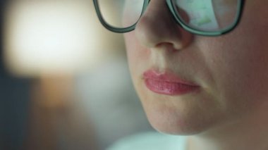Gözlüklü kadın monitöre bakıyor ve çizelgeler ve analizlerle çalışıyor. Monitör ekranı gözlüklere yansıyor. Gece çalış. Aşırı yakın çekim