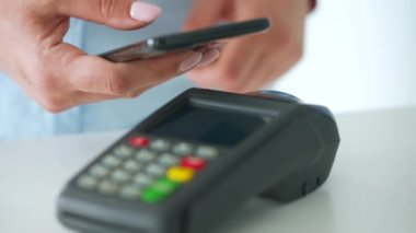 Akıllı telefondan yapılan temassız ödeme. Kablosuz ödeme konsepti. Yakın plan, kadın banka terminalindeki siparişi ödemek için akıllı telefon nakitsiz cüzdan teknolojisi kullanıyor..