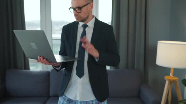 Biały mężczyzna ubrany w kurtkę i bieliznę, korzystający z laptopa, by wykonać wideo rozmowę z domu w nowoczesnym mieszkaniu. Praca zdalna podczas pandemii — Wideo stockowe