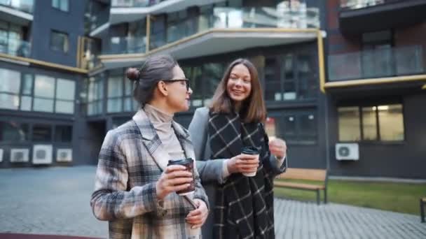 Δύο ευτυχισμένες γυναίκες περπατούν με καφέ και μιλάνε με ενδιαφέρον μεταξύ τους στην επιχειρηματική περιοχή.. — Αρχείο Βίντεο