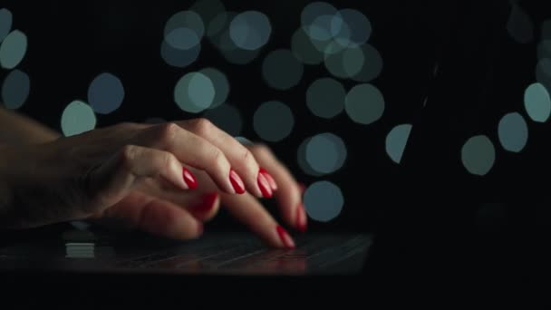 Las manos femeninas están escribiendo en un portátil por la noche. Luces borrosas en el fondo — Vídeo de stock