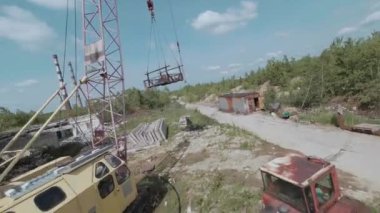 FPV insansız hava aracı, terk edilmiş sanayi binaları ve bir kazıcının etrafında hızla ve manevra kabiliyetiyle uçar..