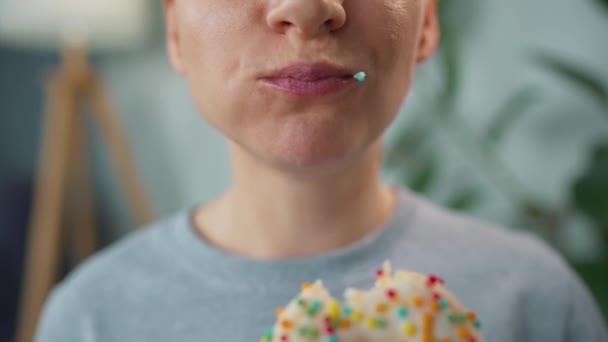 Mujer comiendo una rosquilla dulce en esmalte blanco con aspersiones multicolores. Primer plano — Vídeo de stock