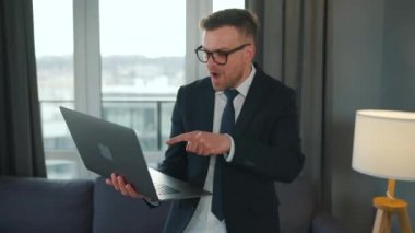 Ceket ve iç çamaşırı giymiş beyaz bir adam modern bir dairede evden video görüşmesi yapmak için dizüstü bilgisayar kullanıyor. Uzaktan çalışmayla ilgili komik video
