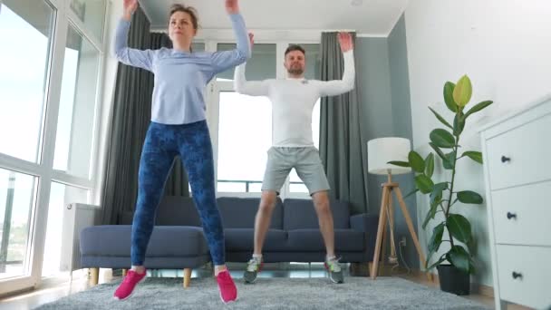 Caucásico pareja está haciendo saltar gatos ejercicio en casa en acogedor habitación luminosa. — Vídeos de Stock
