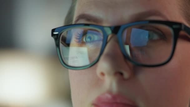Mulher de óculos olhando no monitor e trabalhando com gráficos e análises. A tela do monitor é refletida nos óculos. Trabalho à noite. Extremo close-up — Vídeo de Stock