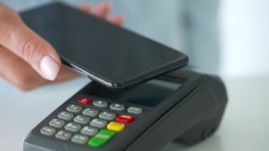 Akıllı telefondan yapılan temassız ödeme. Kablosuz ödeme konsepti. Yakın plan, kadın banka terminalindeki siparişi ödemek için akıllı telefon nakitsiz cüzdan teknolojisi kullanıyor..
