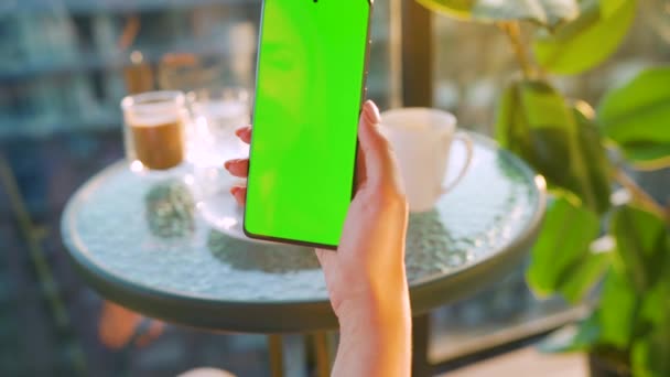 Mujer sentada en un café y usando smartphone con pantalla verde en modo vertical. Chica navegando por Internet, viendo contenido, videos, blogs. — Vídeos de Stock