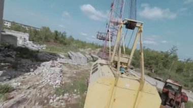 FPV insansız hava aracı, terk edilmiş sanayi binaları ve bir kazıcının etrafında hızla ve manevra kabiliyetiyle uçar..