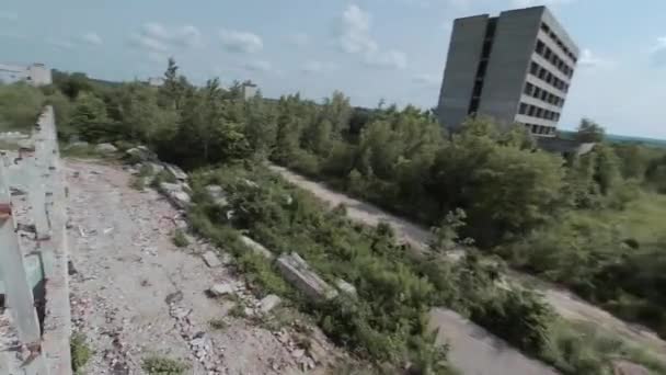 FPV drone vliegt snel en wendbaar tussen verlaten industriële gebouwen en rond een graafmachine. — Stockvideo