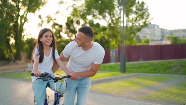 아버지는 딸에게 해 가질 때 자전거타는 법을 가르치고 있다. 느린 동작 — 비디오