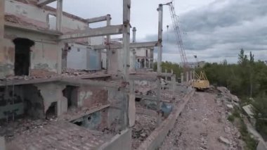 FPV insansız hava aracı, terk edilmiş sanayi binaları ve bir kazıcının etrafında hızla ve manevra kabiliyetiyle uçar..