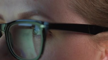 Gözlüklü kadın monitöre bakıyor ve çizelgeler ve analizlerle çalışıyor. Monitör ekranı gözlüklere yansıyor. Gece çalış. Aşırı yakın çekim