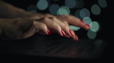 Kadın eller geceleri dizüstü bilgisayarda yazıyorlar. Arkaplanda bulanık ışıklar