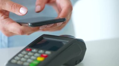 Akıllı telefondan yapılan temassız ödeme. Kablosuz ödeme konsepti. Yakın plan, kadın banka terminalindeki siparişi ödemek için akıllı telefon nakitsiz cüzdan teknolojisi kullanıyor..